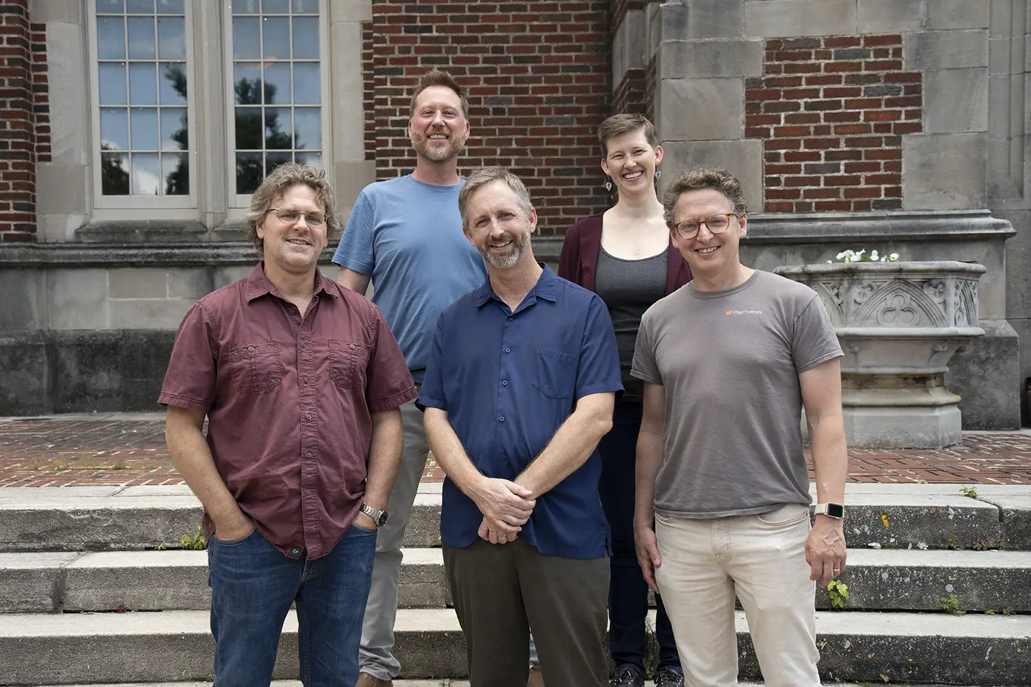 Five faculty members lined up on the steps in front of a brick building