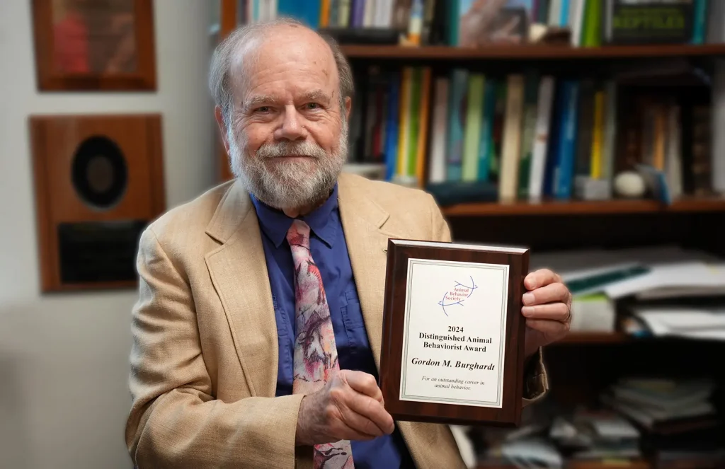 Gordon Burghardt sitting in an office and holding an award